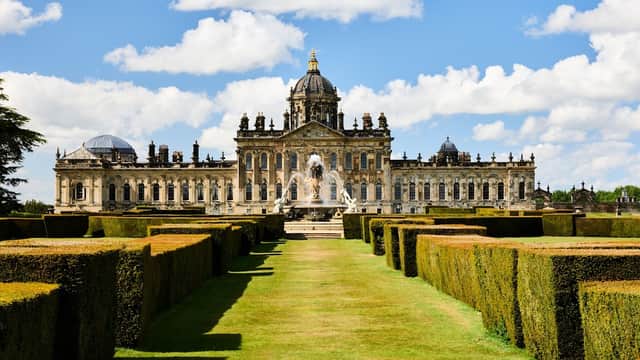 Grand Castle Howard with manicured hedges, a fountain, and a blue sky dotted with clouds in Coneysthorpe, Yorkshire.