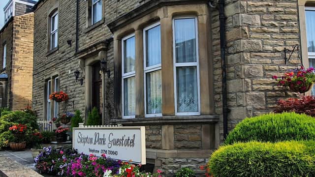 Stone building with large windows, colorful flower beds, and a sign for "Skipton Park Guest'otel" in Bradley, North Yorkshire.