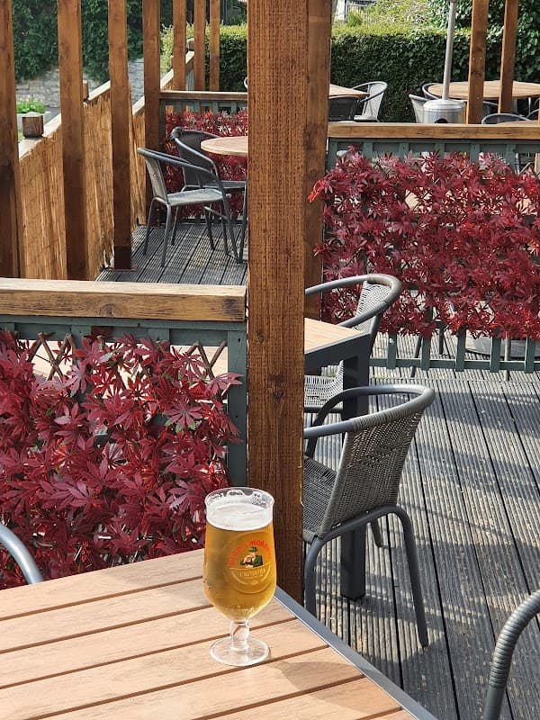 A glass of beer on a wooden table, surrounded by red foliage and outdoor seating at The White Horse restaurant.