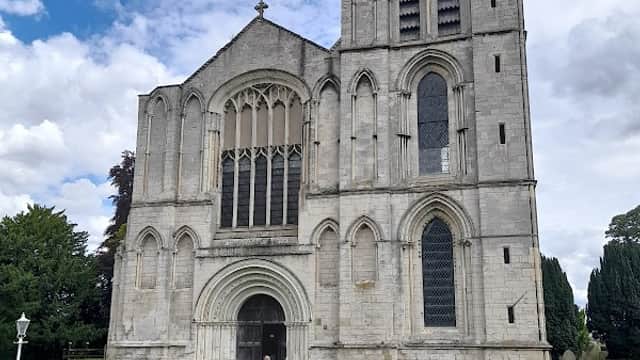 St Mary's Priory Church features a tall stone tower, intricate windows, and a red car parked on the green lawn.