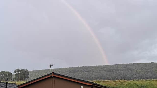 Luxury lodge with wooden exterior, surrounded by greenery and a rainbow arching over a distant hill in Flixton.