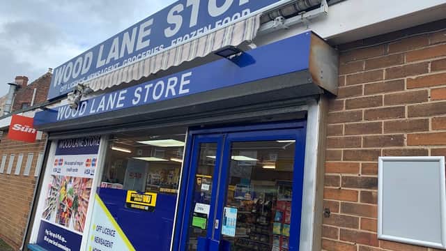 Wood Lane Store storefront featuring a blue sign, large windows displaying various products, and a brick exterior.