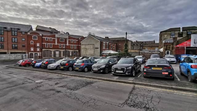 Free parking lot in Tingley, Yorkshire, with various parked cars and buildings in the background under a cloudy sky.