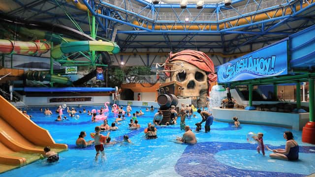 Indoor water park with pirate-themed slides, large skull structure, and families enjoying pools under a glass roof.