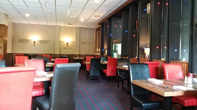 Interior of The Old Poste House Restaurant featuring red and black seating, wooden tables, and ambient lighting.