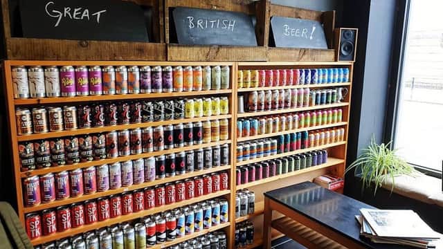 Colorful shelves filled with various beer cans, chalkboard signs reading "Great British Beer!" and a wooden table nearby.