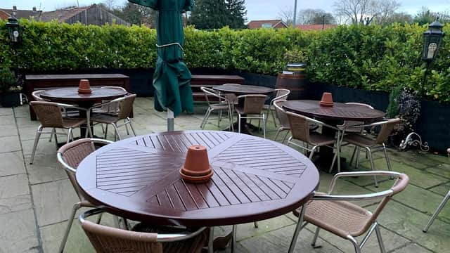 Outdoor seating area with round wooden tables and chairs, surrounded by greenery at The Oak Tree Inn.