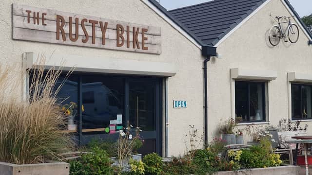Rusty Bike Cafe exterior with wooden sign, open door, bicycle decoration, and planters with greenery.