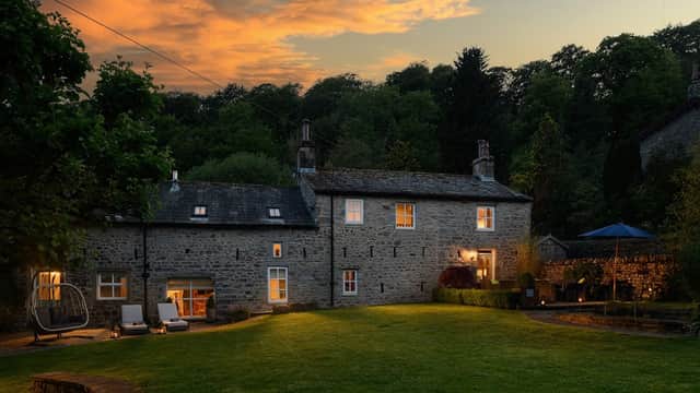 Carrholme Cottage surrounded by lush greenery, with a sunset sky, outdoor seating, and a cozy atmosphere.