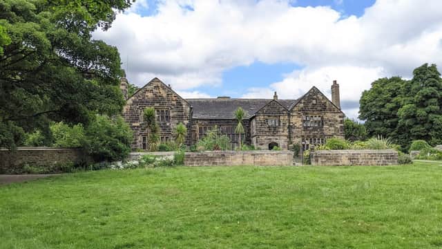 Historic stone building surrounded by lush greenery and trees under a partly cloudy sky.
