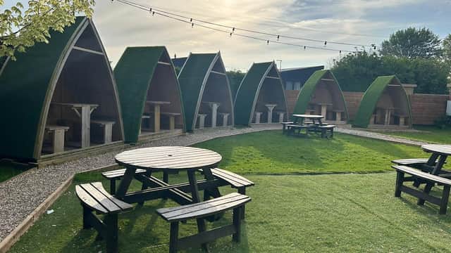 Outdoor seating area with green huts and picnic tables under a bright sky at Black Bull Retreat Bar & Restaurant.