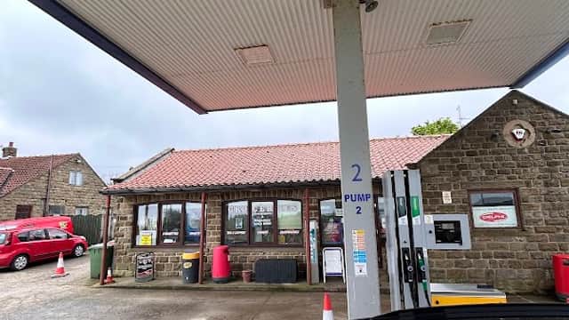 Fylingdales Service Station with stone exterior, fuel pumps, and red vehicles under a cloudy sky.
