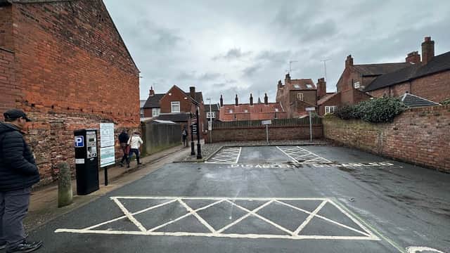Pay & Display car park with empty disabled parking spaces, red brick buildings, and overcast sky in Beverley, Yorkshire.