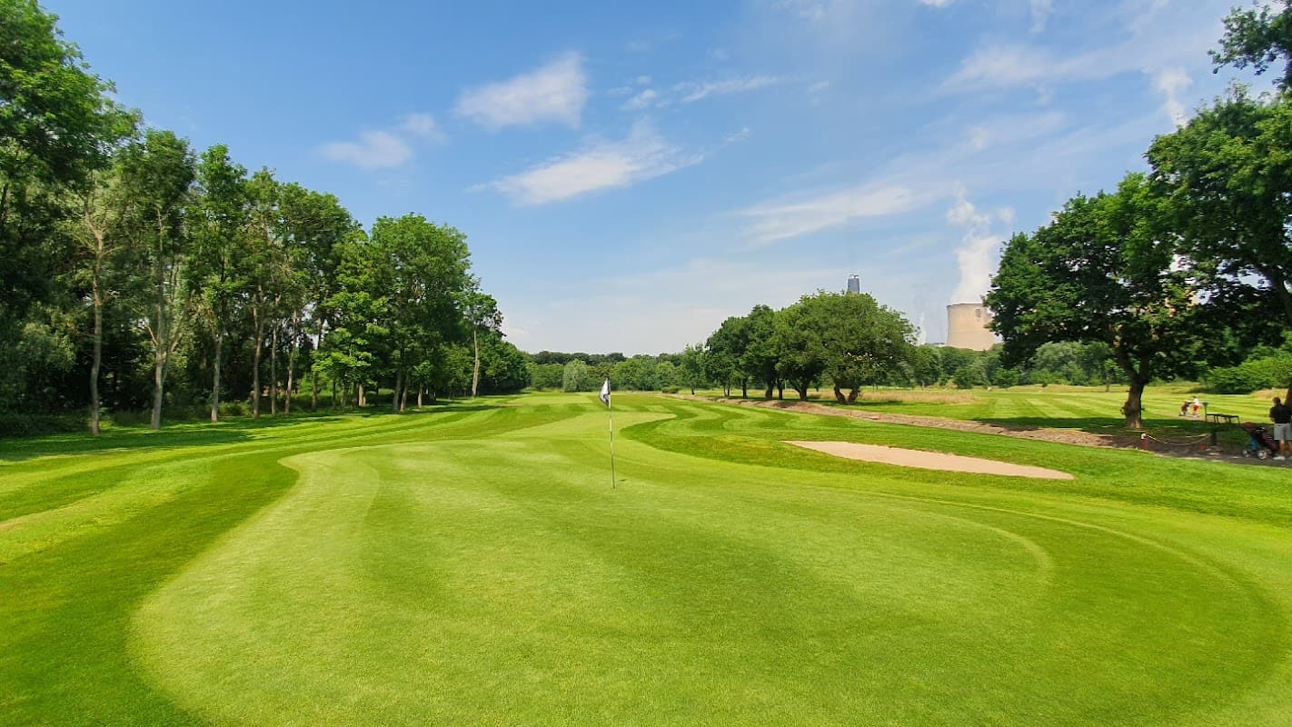 Lush green golf course with rolling fairways, trees, and a sand trap under a clear blue sky in Drax, North Yorkshire.