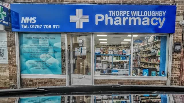 Thorpe Willoughby Pharmacy storefront with blue signage, NHS logo, and window displays of health products.