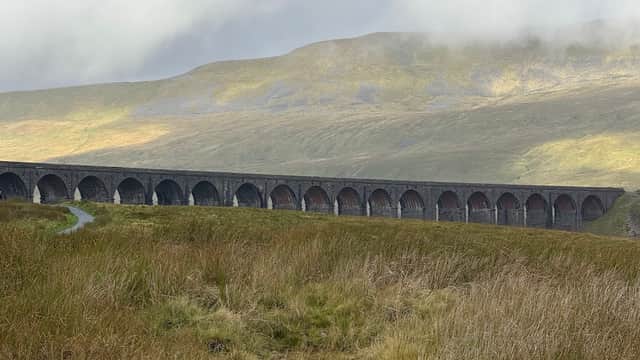 Viaduct spanning a valley, surrounded by grassy hills and misty clouds in Yorkshire Dales National Park.