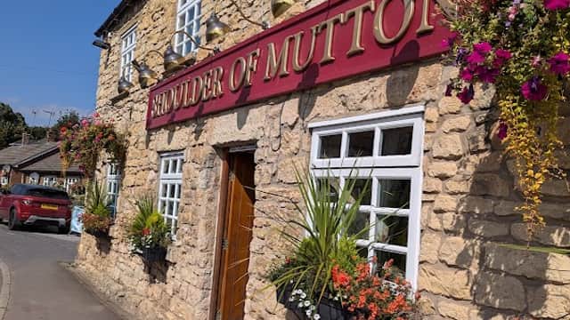 Historic stone pub with red signage, flower baskets, and a sunny blue sky in Kirk Smeaton, Yorkshire.