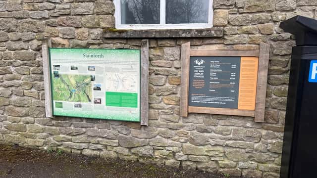 Information boards on a stone wall detailing park maps and Pay & Display charges in Langcliffe, Yorkshire.