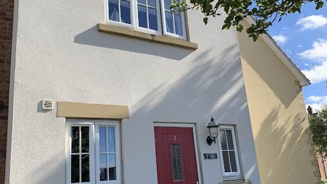 A charming two-story house with a red door, white walls, and a green garden in The Bay, Filey, Yorkshire.