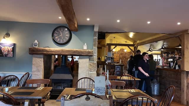 Cozy interior of The Barn with wooden beams, a clock, tables, and patrons at the bar in Winksley, Yorkshire.