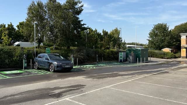 Be.EV Charging Station with electric vehicle parked, green charging spots, and trees in the background.