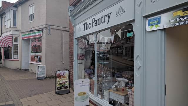 Quaint shopfront of "The Pantry" with decorative bunting, showcasing a variety of baked goods and a cozy atmosphere.