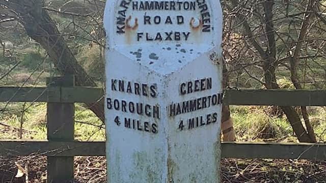 Weathered stone milestone with distances to Knaresborough, Green Hammerton, and Flaxby, surrounded by trees.