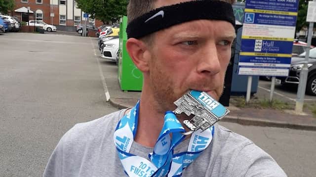 A man wearing a headband and a Georgetown t-shirt holds a medal in his mouth, standing in a car park.