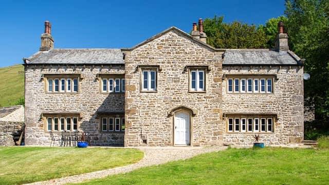 Stone building with large windows, set in a green landscape, featuring a black dog resting on the grass.
