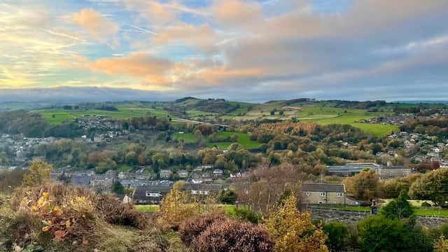 Lush green hills and valleys under a colorful sky, with a quaint village nestled below in Holmfirth, Yorkshire.