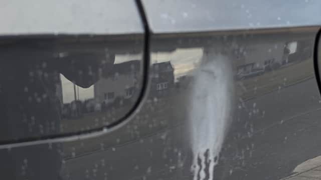 A close-up of a car's side, showing a streak of white substance against a dark surface.