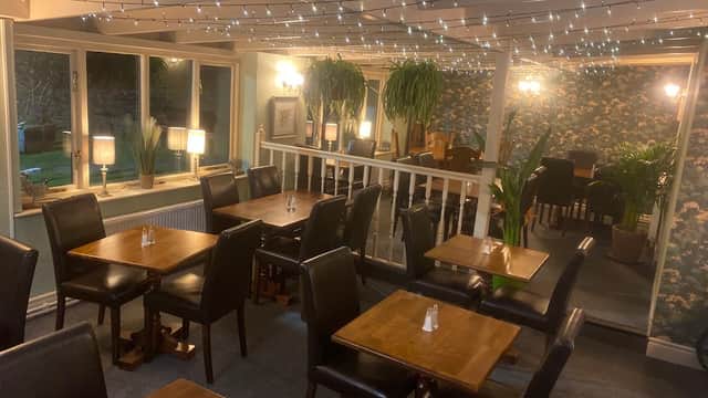 Cozy restaurant interior with wooden tables, black chairs, string lights, and lush plants in Downholme, Yorkshire.