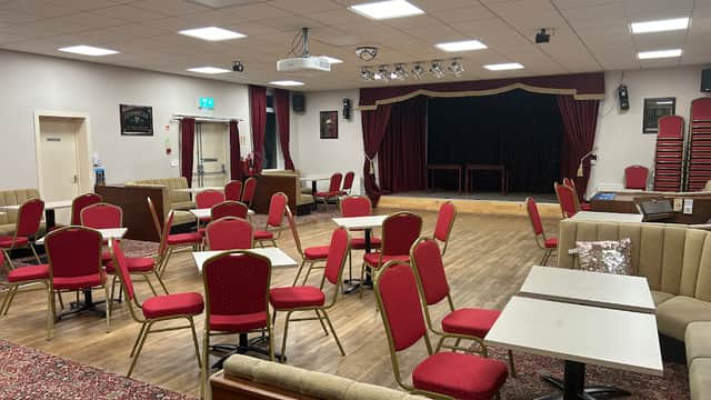 Interior of Scissett Club Ltd with red chairs, tables, a stage, and a carpeted floor in a cozy setting.