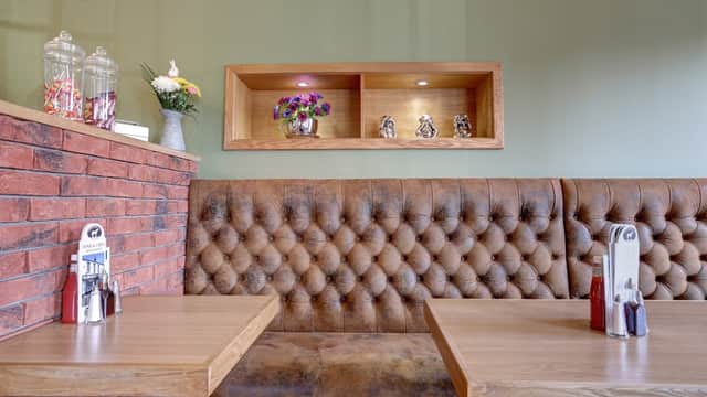 Cozy takeaway interior with tufted brown seating, wooden tables, and decorative shelves with flowers and figurines.