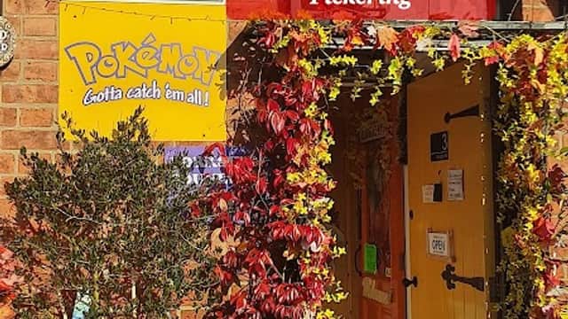 Colorful storefront of Aladdin's Cave Gifts & Gaming, adorned with flowers and signs, in Pickering, Yorkshire.
