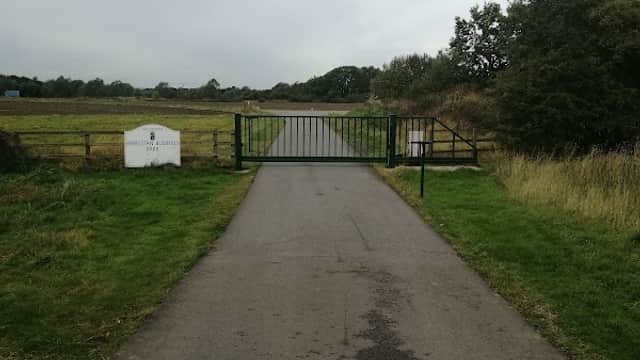 A gated entrance to Athelstan Business Park, with a gravel path leading through grassy fields under a cloudy sky.