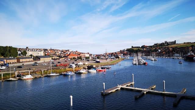 View of Whitby Coach Park with parked vehicles, boats in the harbor, and a scenic coastline under a blue sky.