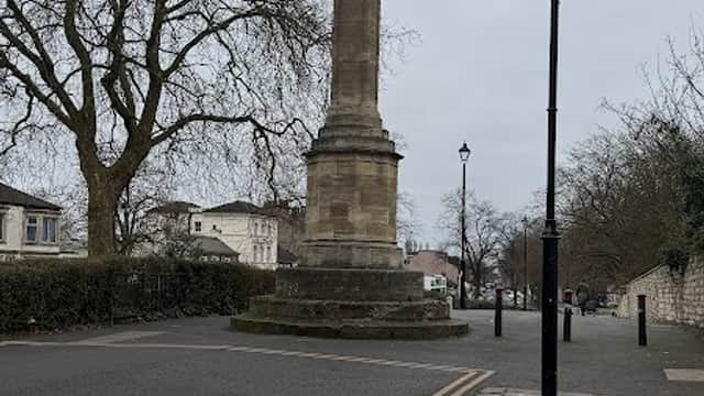Stone column with a weather vane, surrounded by trees and lampposts on a cobblestone street in Doncaster.
