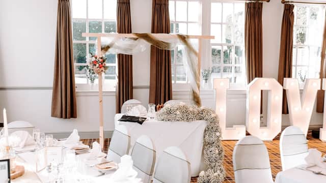 Elegant floral arrangements with a decorative arch and illuminated "LOVE" sign in a bright, stylish venue.