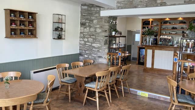 Cozy café interior with wooden tables, chairs, stone walls, and a counter adorned with plants and displays.
