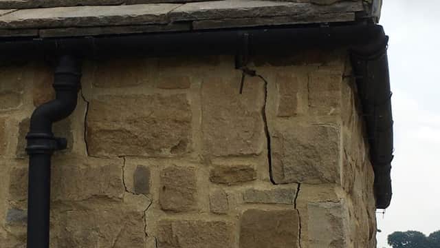 Cracked stone wall with a downpipe, near the roofline of a building in Huby, Yorkshire.