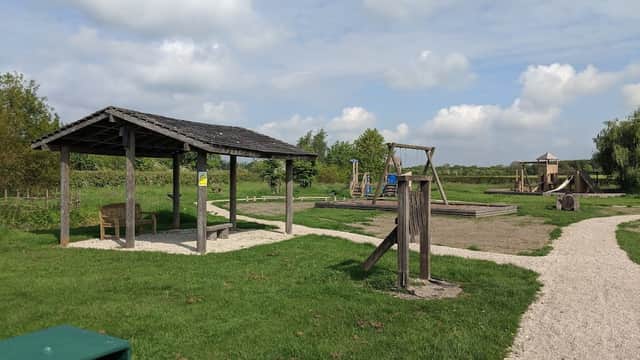Wooden shelter with benches, swings, and play structures under a blue sky with fluffy clouds in Jubilee Park, Fangfoss.