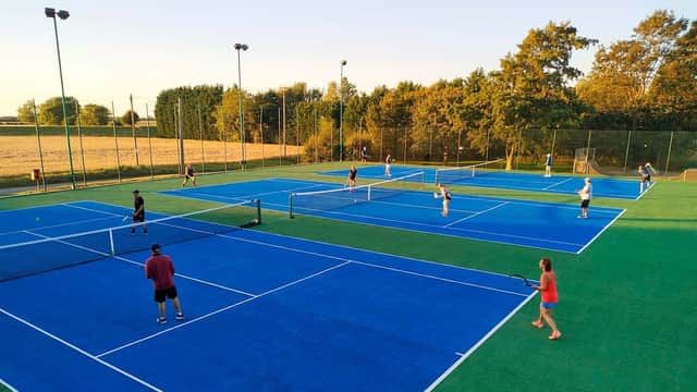 Several players engage in tennis on vibrant blue courts surrounded by greenery at Wistow Tennis Club.