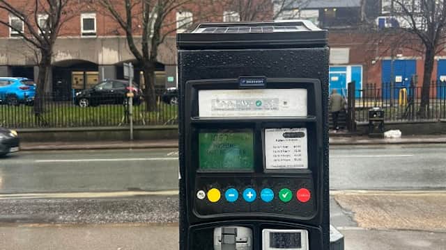 Pay & Display parking meter with buttons and screen, in front of a brick building and tree-lined street in Killingbeck.