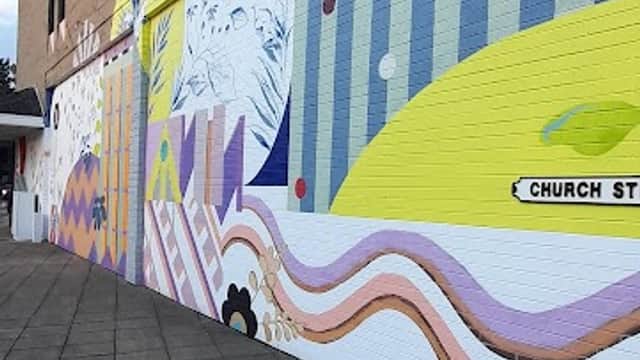 Colorful mural on a building wall, featuring abstract shapes and patterns, with a paved walkway in the foreground.
