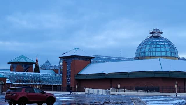 Snow-covered parking lot with a modern building featuring a glass dome and green roofs in a cloudy sky.