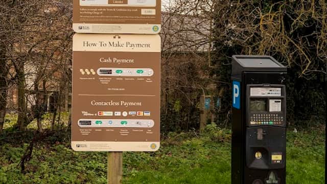 Signage for a pay & display car park with payment instructions and a parking machine in a grassy area.