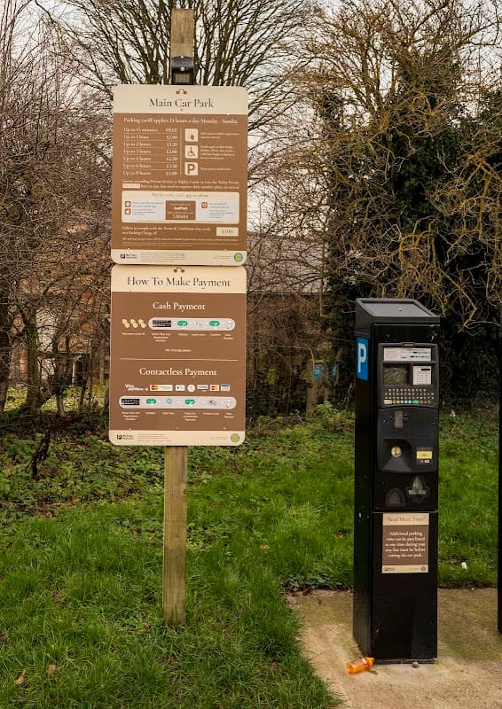 Signage for a pay & display car park with payment instructions and a parking machine in a grassy area.