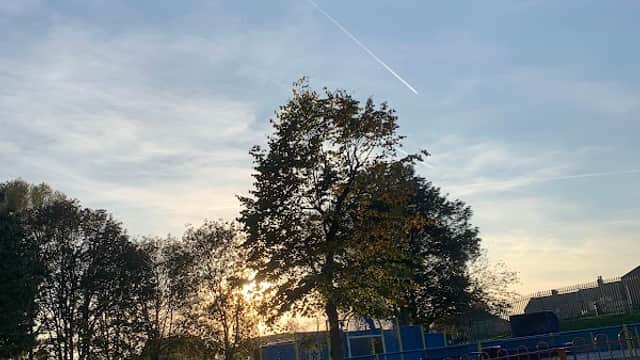Sunset view over Mapplewell Park, featuring trees, a grassy area, and playground equipment in the background.