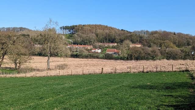 Cholmeley Hall nestled in a rural landscape, surrounded by fields and trees under a clear blue sky.